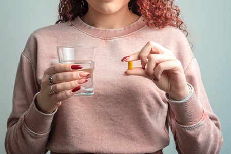 Midsection of woman in pink sweatshirt holding tablet and water