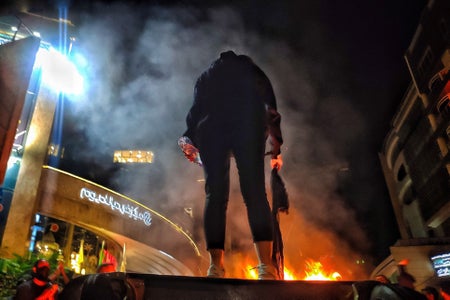 Low angle, rear view of woman in silhouette holding scarf with fire seen in background