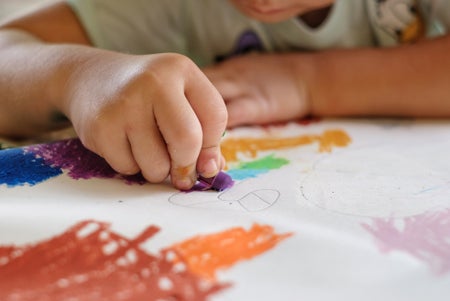 Close up view of a child's fingers coloring with crayons.