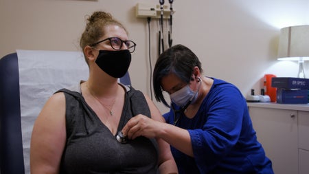 A young woman in a mask and glasses is examined by a doctor.