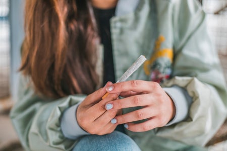 Teenager with chipped light blue nail polish holding a joint.