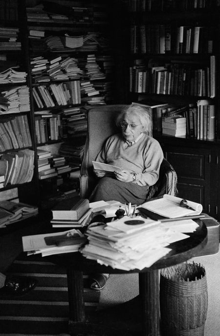 Albert Einstein sitting at desk behind stack of paper.