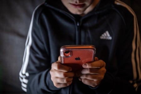 Teenager with blue sports jacket holding orange cased iphone.