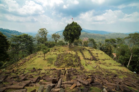 Megalithic site on hilltop with stones in foreground and centered tree looking into a valley.