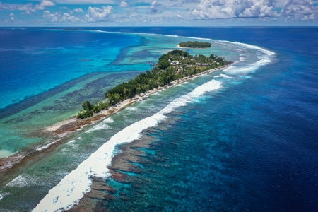 Aerial view of Tuvalu, picturing a narrow island, ocean, palm trees, waves