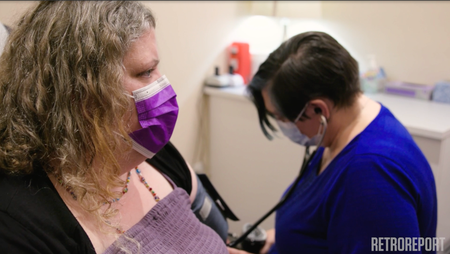 A women in a mask being seen in a doctor's office.